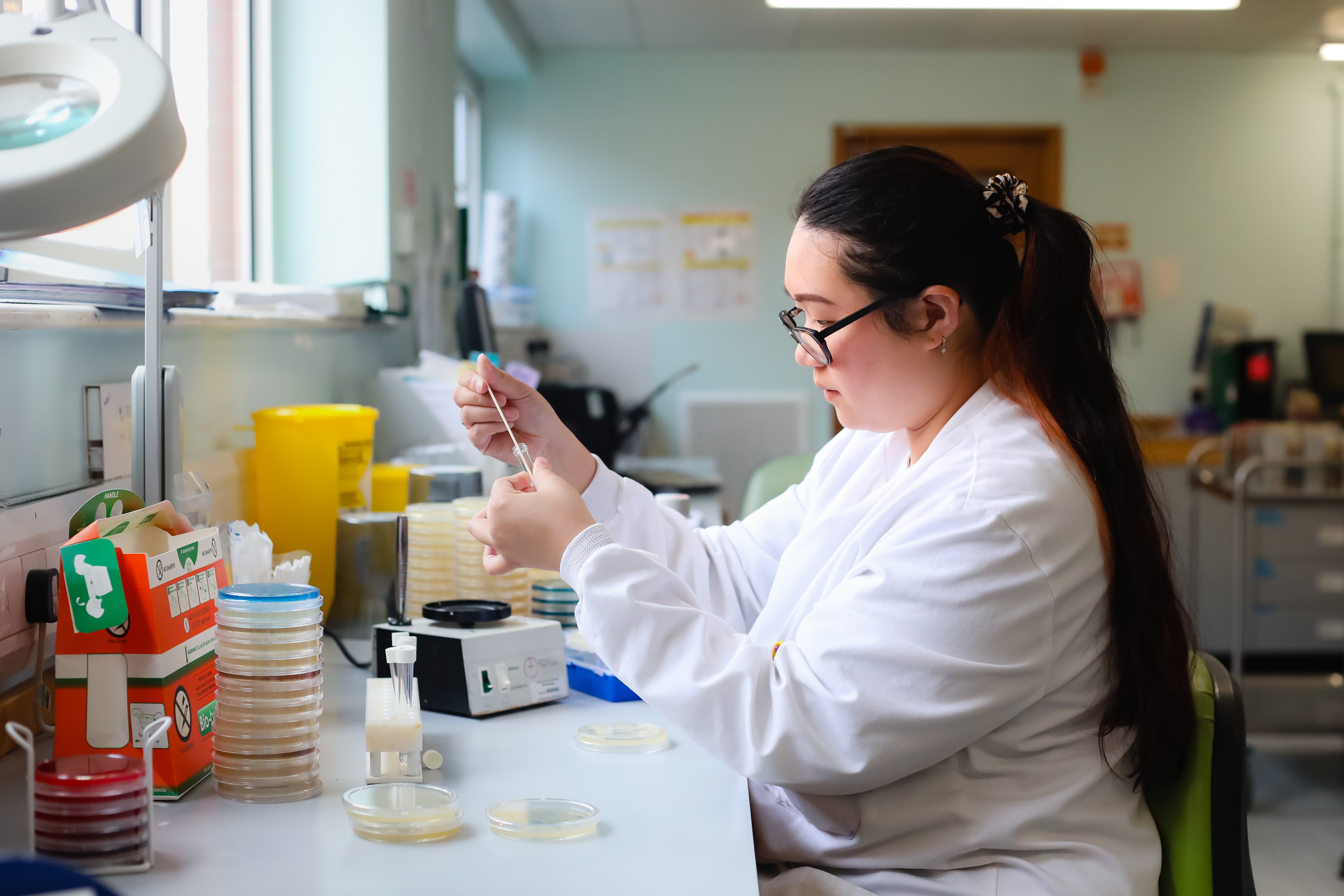 A Morecambe Bay NHS colleague in a white lab coat sat at a desk carrying out a lab test with a test tube