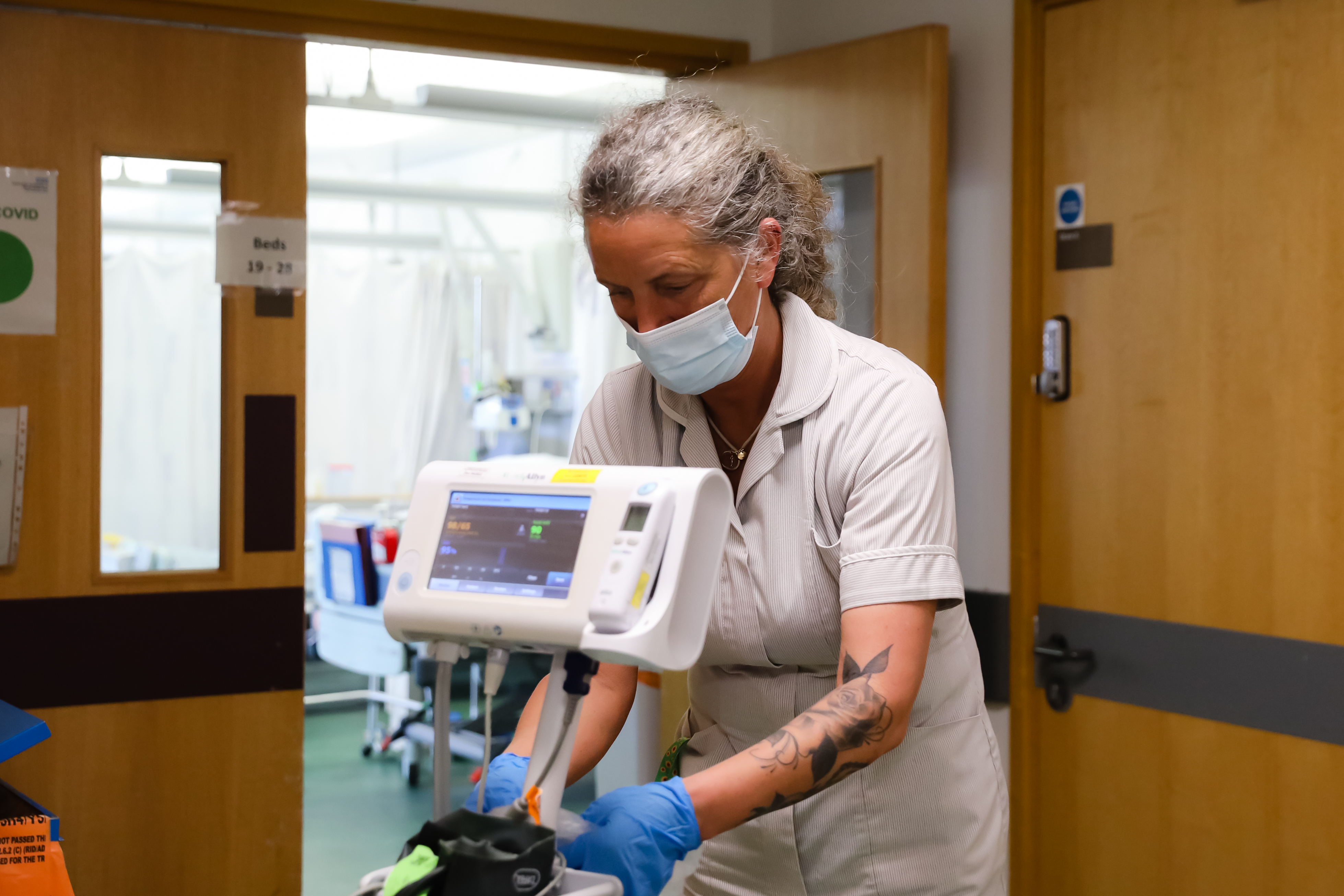 A Morecambe Bay NHS colleague in white uniform and blue gloves using a patient monitoring machine